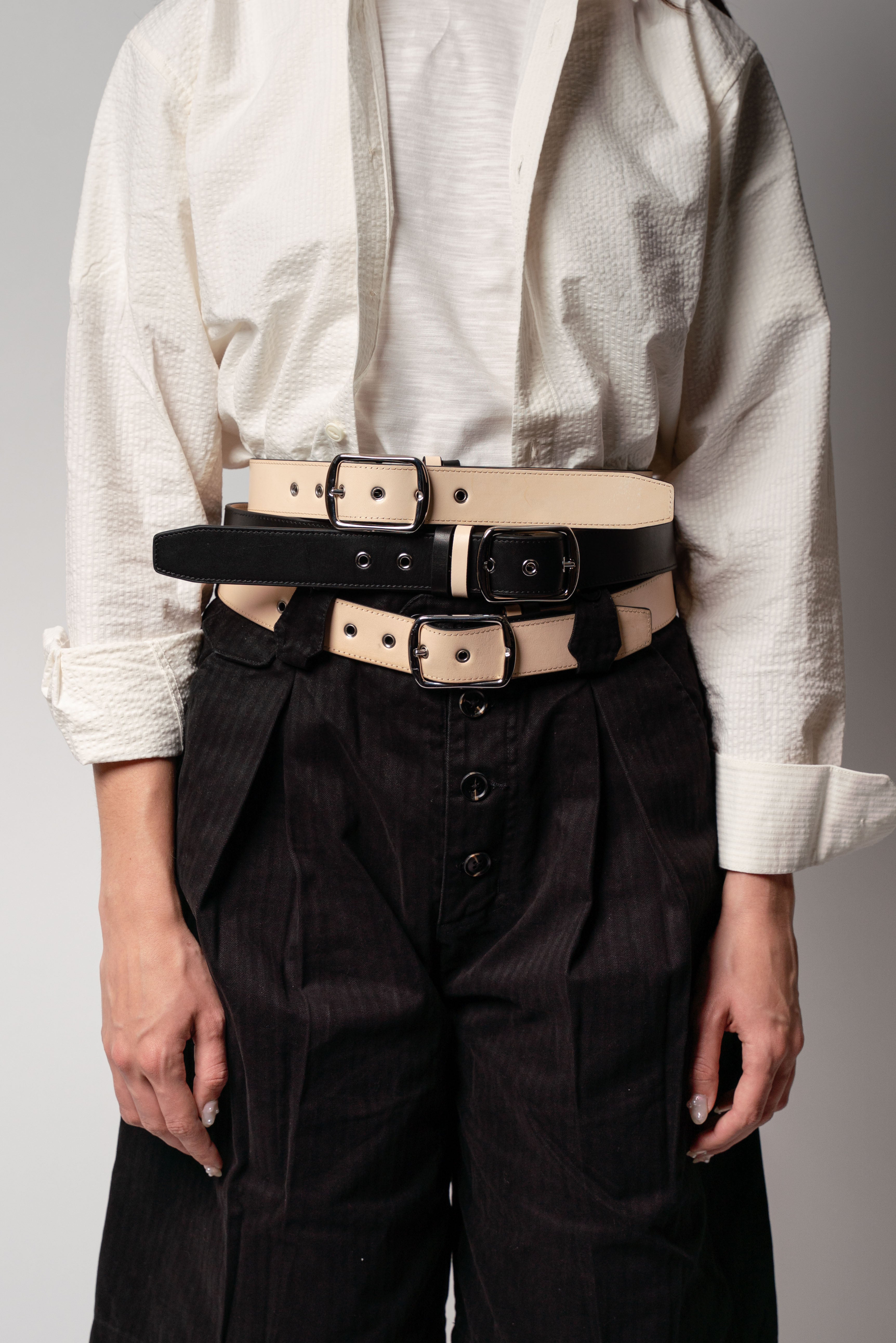 Person wearing a white shirt and black pants with multiple belts around the waist on a gray background