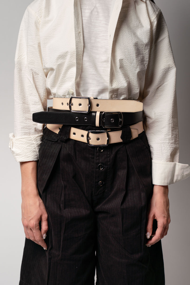 Person wearing a white shirt and black pants with multiple belts around the waist on a gray background